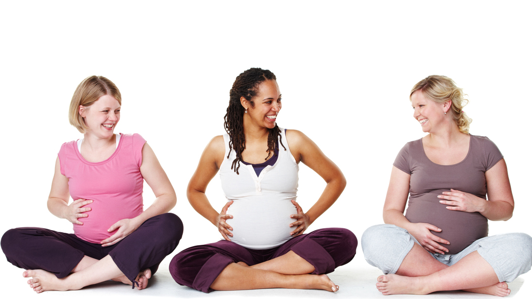 3 smiling pregnant women, in fitness clothes, sitting cross-legged on fitness mat