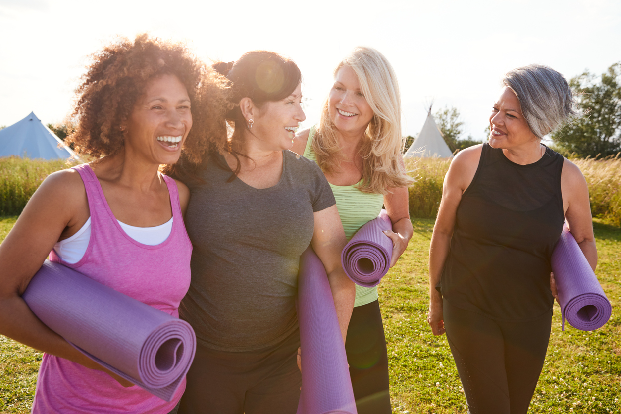 A group of women dressed in fitness clothes, smiling and talking, walking to an outdoor exercise class