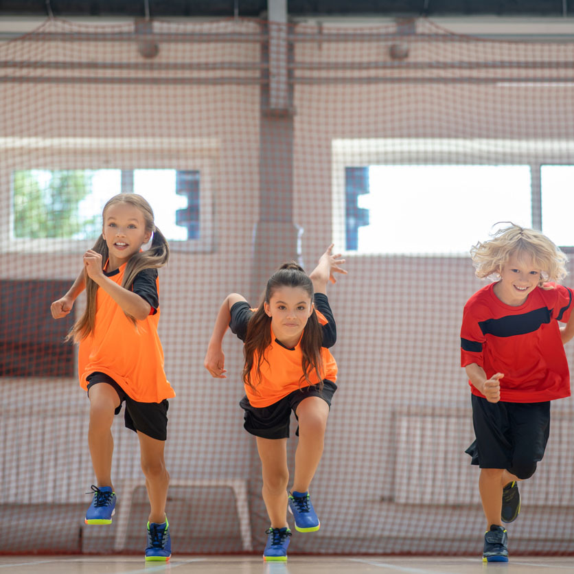 Three kids having fun running fast across a gym floor